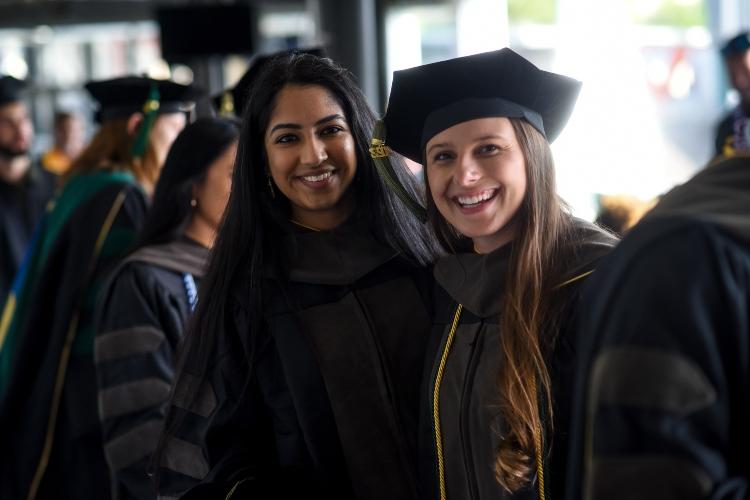 Two women in graduation robes smile